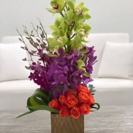 Tall orchid arrangement with orange roses in a wooden vase