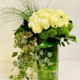 White roses arranged in a clear rectangular vase with trailing greenery