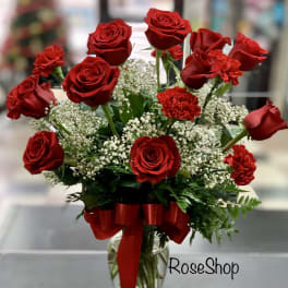 Red roses and carnations arranged in a glass vase with a red ribbon