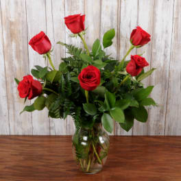 Six red roses in a clear glass vase on a wooden table