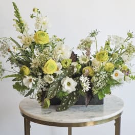 Low floral arrangement with yellow and white blooms in a black container