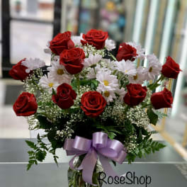 Red roses and white daisies in a glass vase with a lavender ribbon