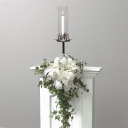 White lily arrangement with trailing greenery and a lit candle in a glass holder