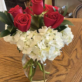 Red roses and white hydrangeas arranged in a clear glass vase