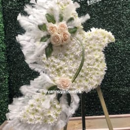Angel-shaped standing spray of white flowers with blush roses and feathers on a metal easel