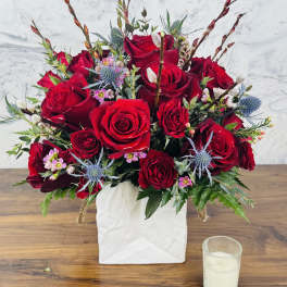 Red rose arrangement in a white square vase with blue thistle accents