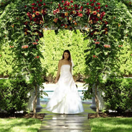 Outdoor wedding arbor covered in greenery with red and orange flowers over a stone path