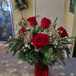 Red roses arranged in a red glass vase with white filler flowers
