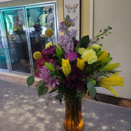 Mixed bouquet of purple, yellow, and pink flowers in an amber glass vase