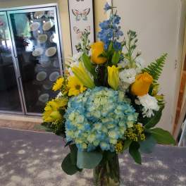 Blue hydrangeas with yellow roses and white flowers in a glass vase