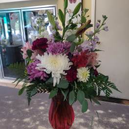 Mixed bouquet of white, pink, and purple flowers in a red glass vase