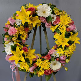 Circular floral wreath with yellow lilies, pink roses, and white daisies on an easel