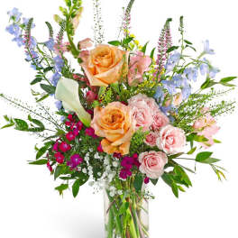 Mixed bouquet of roses, calla lilies, and blue flowers in a glass vase