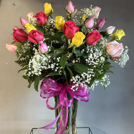 Bouquet of multicolored roses in a clear glass vase with a pink ribbon