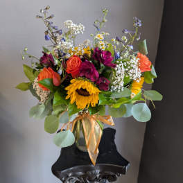 Mixed bouquet with sunflowers, roses, and purple blooms in a glass vase