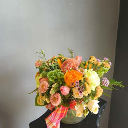 Mixed bouquet of orange, pink, and cream flowers in a vase with a plaid ribbon