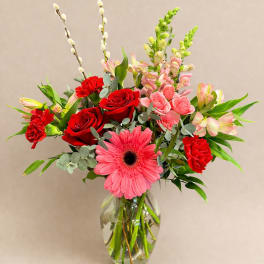 Mixed bouquet with red roses, pink gerberas, and carnations in a glass vase