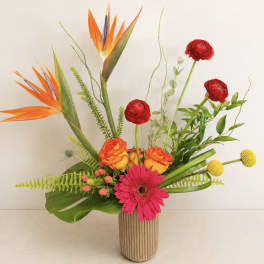 Tropical bouquet with orange bird-of-paradise, red ranunculus, and pink gerbera in a ribbed vase