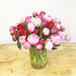 Pink and red tulips and peonies in a clear glass vase
