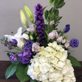 Purple and white floral arrangement with lilies, roses, and hydrangeas in a glass vase