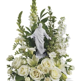 White roses and lilies arranged around a small religious statue