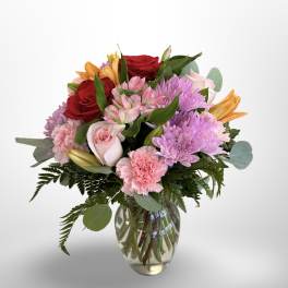 Mixed bouquet of roses, lilies, carnations, and chrysanthemums in a glass vase