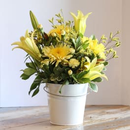 Yellow lilies and daisies in a white metal bucket