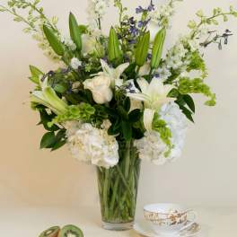 White lilies and roses in a glass vase with kiwi and a teacup