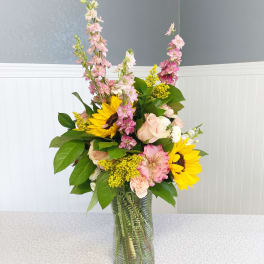Mixed bouquet with sunflowers, pink blooms, and a glass vase