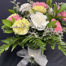 Bouquet of pink, yellow, and white carnations in a glass vase with a ribbon