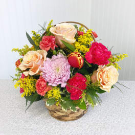 Basket arrangement of peach roses, pink carnations, and a lavender chrysanthemum