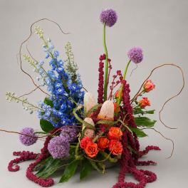 Tall floral arrangement with blue, purple, and orange blooms in a low container