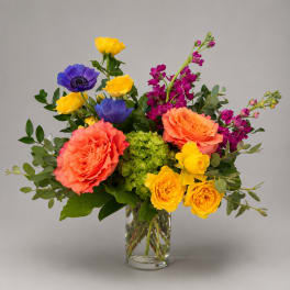 Colorful bouquet of roses, anemones, and orchids in a clear glass vase