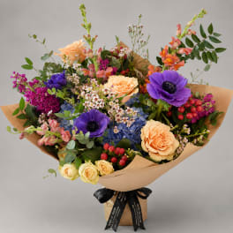 Mixed bouquet with purple anemones, peach roses, and blue hydrangeas in kraft paper