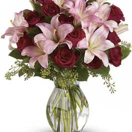 Arrangement of pink lilies and red roses in a clear glass vase