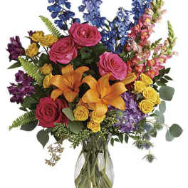 Tall mixed bouquet of pink roses, orange lilies, and bright assorted blooms in a clear glass vase.