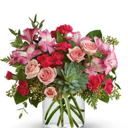Pink roses and carnations in a clear glass vase with a succulent center