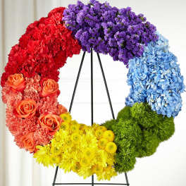 Rainbow floral wreath on a black stand with roses, carnations, hydrangeas, and mums