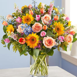 Mixed bouquet of sunflowers, roses, and tulips in a glass vase