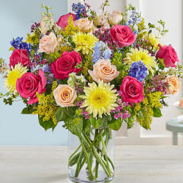 Mixed bouquet of roses, daisies, and blue flowers in a clear glass vase