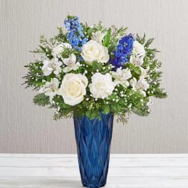 White roses and blue flowers arranged in a tall blue vase