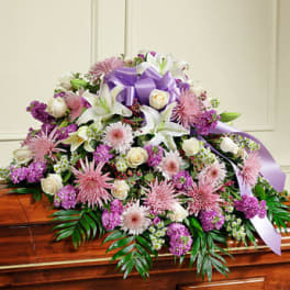 Large white and pink floral spray with a purple ribbon on a casket