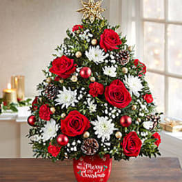 Christmas tree-shaped floral arrangement with red roses and white flowers in a red pot