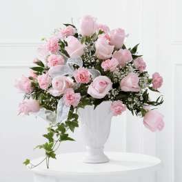 Pink roses and carnations in a white vase with a sheer ribbon