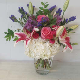 Mixed bouquet of pink roses, lilies, and white hydrangea in a glass vase