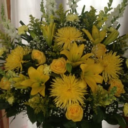 Yellow lilies and roses arranged with white snapdragons in a large display.