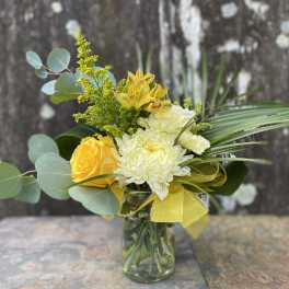 Yellow and white flower arrangement in a glass vase with ribbon