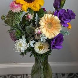 Mixed bouquet with sunflowers, purple blooms, and daisies in a glass vase
