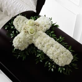 White floral cross with roses resting on a dark casket