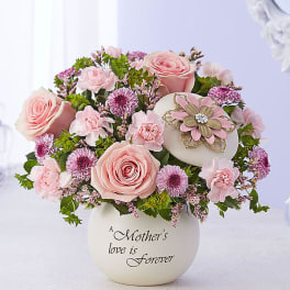 Pink roses and carnations in a white vase with a decorative flower accent
